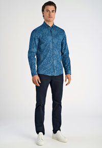 Langarmige blauwe shirt met een textuur van een bladerenpatroon, knoopsluiting en een klassieke kraag, gecombineerd met donkere broeken en witte sneakers.