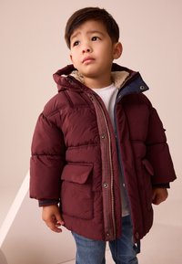 Doudoune bordeaux avec capuche, fermeture éclair, deux poches avant et doublure en polaire autour du col. Manches courtes et tissu texturé.