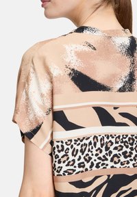 Blouse à manches courtes en beige avec des motifs abstraits, y compris des rayures de zèbre et un imprimé léopard, offrant une coupe décontractée et une texture douce.