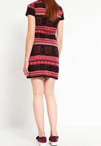 Robe à manches courtes avec une base noire arborant un motif rose et rouge, en tissu doux et avec une coupe ajustée. Portée avec des chaussures bordeaux.