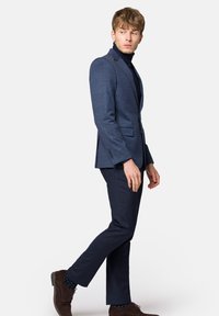 Ciemnoniebieska marynarka w kratę z klapami w kształcie notcha, zestawiona z dopasowanymi spodniami i brązowymi butami, noszona na czarnym golfie.