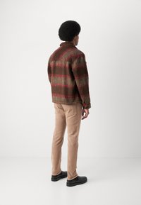 Wollen plaid jack in bruin en rood, met een puntige kraag en zijzakken, gecombineerd met lichtbruine broek en zwarte schoenen.