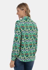 Ilgų rankovių marškiniai su žaliai raštuota apdaila, akcentuota oranžine, mėlyna ir balta spalvomis. Pagaminti iš lengvos medžiagos, su laisvu siluetu.