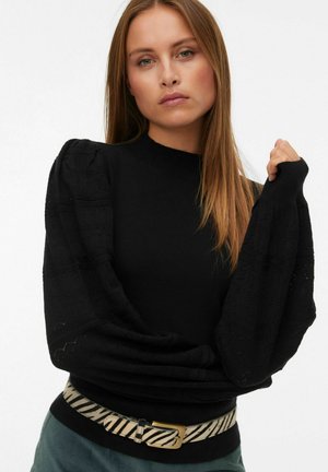 Pull noir avec des manches bouffantes texturées, présentant un col côtelé. Porté avec une large ceinture rayée. Design simple et élégant.