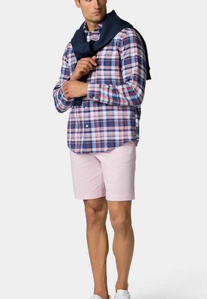 Geruit blauw en rood overhemd, roze shorts, en een marineblauwe sweater over de schouders gedrapeerd. Bevat knoopdetails en een ontspannen pasvorm.