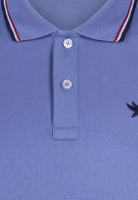 Camisa polo de color azul claro con tejido texturizado, tapeta de tres botones y cuello con franjas rojas y marinas. Acento de logo negro.