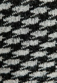 Gebreide stof met een houndstoothpatroon in zwart en wit, met een zachte textuur en duidelijke garenstrengen die door het geheel zichtbaar zijn.