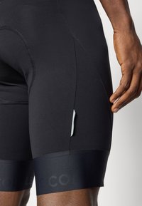 Schwarze Sportshorts mit figurnahem Schnitt und strukturiertem Stoff. Verfügt über ein dezentes Logo am Bund und einen kleinen reflektierenden Akzent an der Seite.