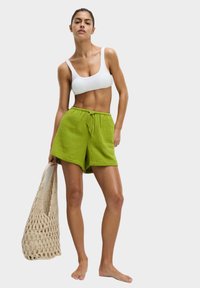 Groene textuurshorts met een elastische taille en strikdetail, gecombineerd met een witte geribbelde crop top. Draagt een crèmekleurige geweven tote bag.