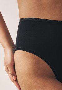 Mutandine nere a vita alta con una texture liscia, caratterizzate da una fascia con logo discreto e cuciture pulite lungo i bordi.