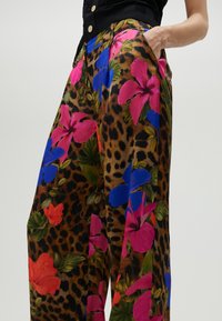Wijdvallende broek met een luipaardprint als basis, versierd met grote roze, blauwe en rode bloemmotieven. Gemaakt van lichte stof met zakken.