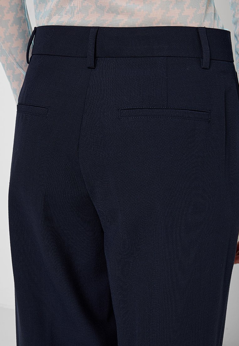 Marineblaue Hose aus strukturiertem Stoff mit flachem Bund und zwei Gesäßtaschen, ohne sichtbare Verschlüsse oder Muster.