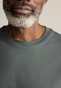 Tricou gri închis cu guler rotund, dintr-un amestec de bumbac, având o textură netedă, fără modele sau accente vizibile. Vedere detaliată a gulerului.