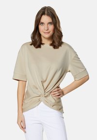 Beige korte mouwen shirt met een geknoopte voorkant, gemaakt van zachte stof. Gepaarde met witte broek, met een ontspannen pasvorm.