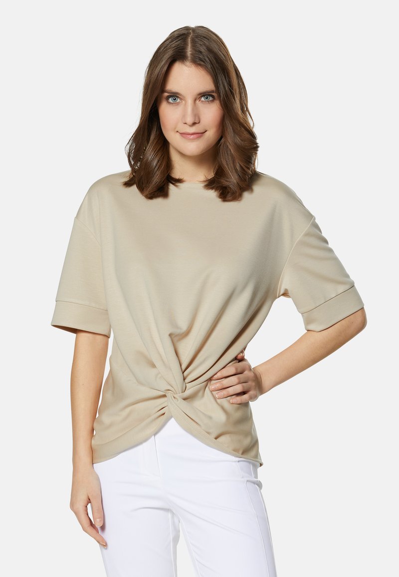Beige korte mouwen shirt met een geknoopte voorkant, gemaakt van zachte stof. Gepaarde met witte broek, met een ontspannen pasvorm.