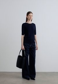 Ναυτικό μπλουζάκι με κοντά μανίκια, συνδυασμένο με φαρδιά τζιν παντελόνια σε σκούρο χρώμα. Μαύρη τσάντα με στρογγυλή λαβή και γεωμετρικό σχήμα. Απλός, μοντέρνος σχεδιασμός.