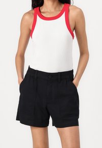 Bílý kanálkový top s červenými detaily, spárovaný s černými šortkami na elastický pas s bočními kapsami a knoflíkovým zapínáním.
