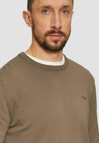 Brown knitted sweater with a round neckline, featuring a subtle logo on the chest. Smooth texture with a fitted design.