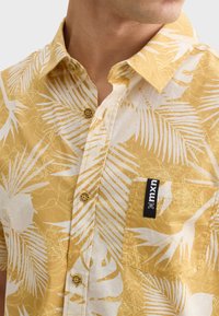 Korte mouwen overhemd in lichtgeel met witte tropische bladerenpatronen, voorzien van een button-down kraag en een borstzak met logo label.