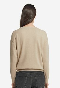 Beige gestrickter Pullover mit lockerer Passform, weitem Bootsausschnitt und langen Ärmeln. Weiche Textur mit gerippten Bündchen und Saum.