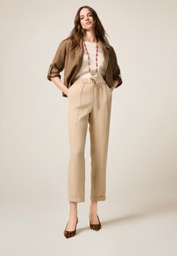Pantalons beige ajustés avec taille à cordon, associés à un haut blanc et une veste rayée marron. Complétés par des escarpins à imprimé léopard.