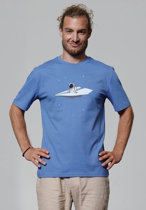 Blauwe katoenen t-shirt met een grafisch ontwerp van een astronaut op een papier vliegtuig, tegen een eenvoudige sterrenachtergrond. Korte mouwen, ronde hals.