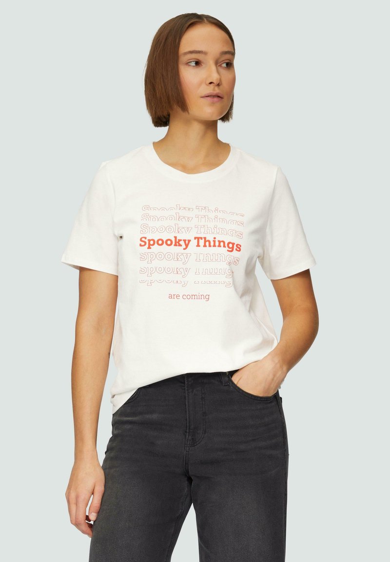 Witte katoenen T-shirt met rode en grijze tekst die "Spooky Things are coming" in verschillende lettertypes zegt. Dragen met donkergrijze jeans.