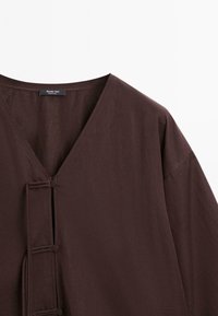 Vêtement marron foncé à col en V avec boutons recouverts de tissu et boucles sur l'avant, fabriqué par Massimo Dutti.