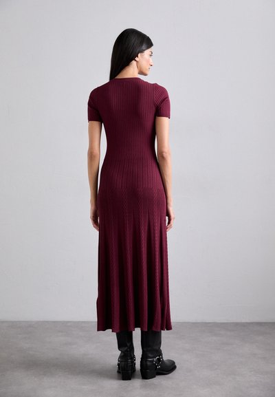 Burgundijas ribota midi kleita ar īsām piedurknēm, pieguļošs augšdaļa, izvērstā svārku daļa un teksturēts dizains; saskaņota ar melniem potīšu zābakiem ar sprādzēm.