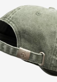 Zielona czapka z aksamitu sztruksowego z zakrzywionym daszkiem, wyposażona w metalowe zapięcie na pasku oraz akcent z logo marki. Materiał o fakturze z delikatnymi detalami przeszyć.