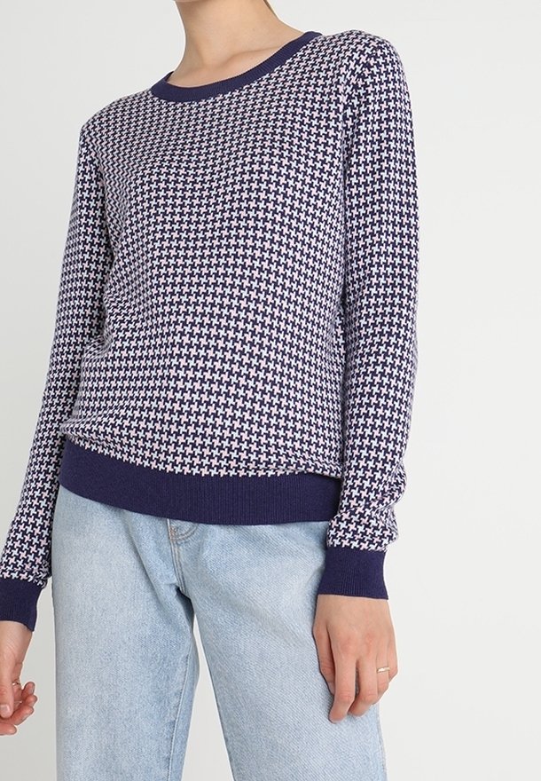 Námorně modrý pletený svetr s geometrickým vzorem, kulatým výstřihem a náplety; spuštěný s světle modrými rovnými džíny.