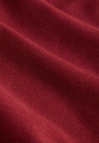 Textúrovaná bordová tkanina s jemným, hladkým povrchom, obsahujúca jemné variácie v farbe a zrne, vhodná na odevy alebo čalúnenie.