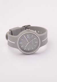 Reloj de pulsera de silicona gris con una correa texturizada, esfera redonda, marcadores de hora plateados y una pequeña corona. Presenta un sutil acabado brillante.