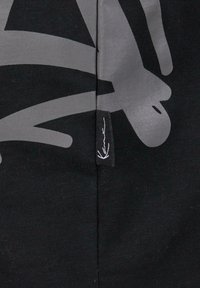 Black fabric featuring a large gray graphic design. A small tag with a logo is visible along the seam. Soft texture, casual style.