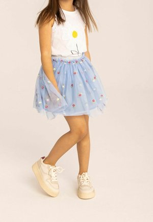 Top blanco sin mangas con estampado de margaritas, combinado con una falda de tul azul claro con bordados florales y zapatillas en color crema.