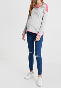 Harmaa pitkähihainen paita, jossa vaaleanpunaisia yksityiskohtia, yhdistettynä sinisiin revittyihin skinny-farkkuihin ja valkoisiin tennareihin. Pehmeä kangas, rento istuvuus.