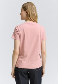 Camiseta de algodón rosa con mangas cortas, cuello redondo y una textura suave. Combinada con jeans de mezclilla oscuros, vista desde la parte de atrás.