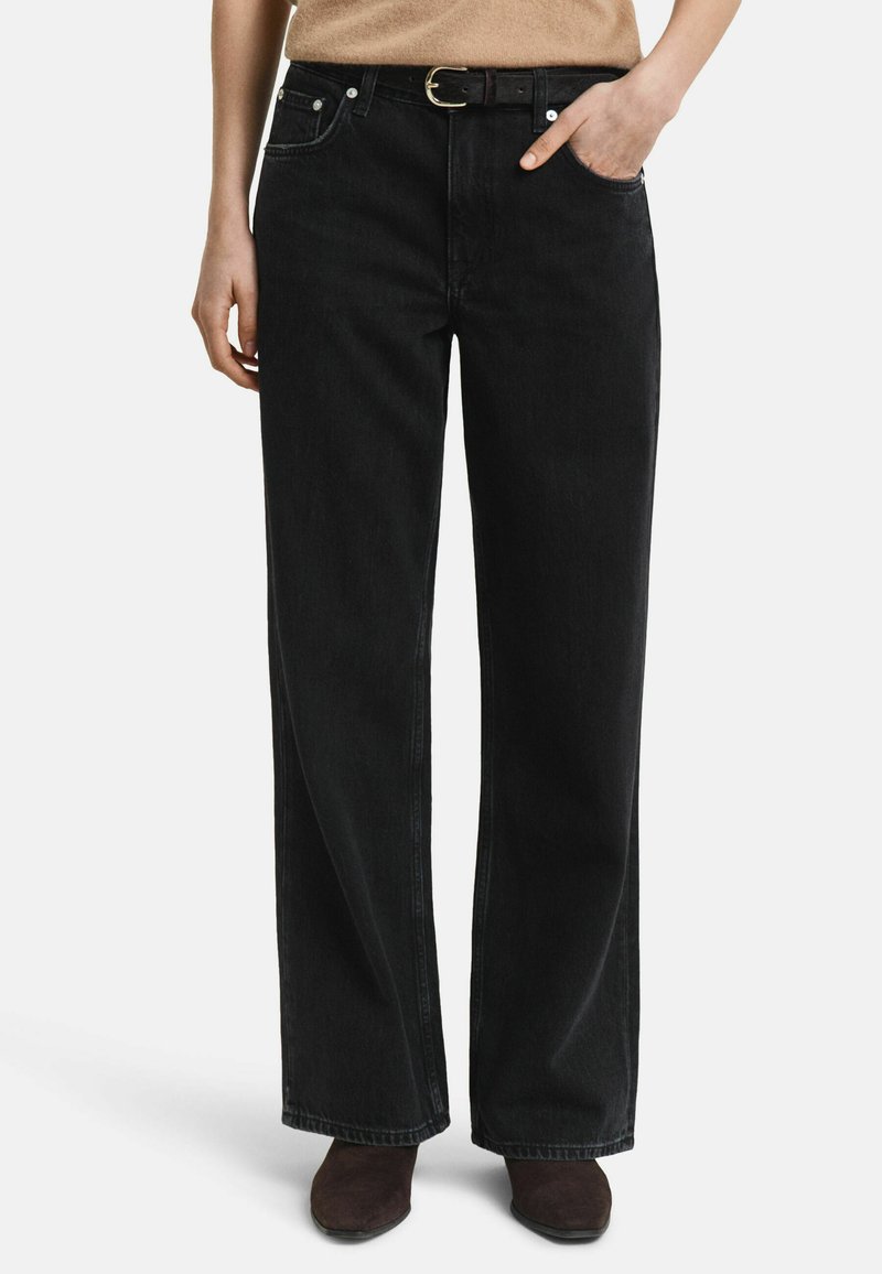 Jean large noir à taille haute, doté de poches avant, de quincaillerie métallique et d'une ceinture visible avec une boucle en or.