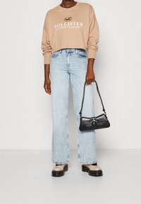 Beige zkrácená mikina se potiskem "Hollister Southern California", světle modré široké džíny, černá kabelka a béžové platformové boty.