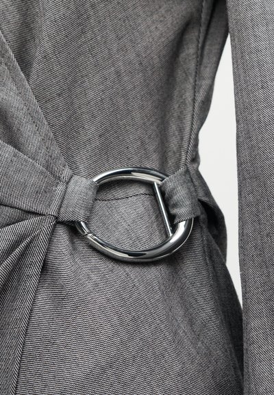 Κοντινό πλάνο γκρι υφασμάτινης ζώνης σφιγμένης με γυαλιστερή ασημένια στρογγυλή μεταλλική αγκράφα σε ένδυμα.