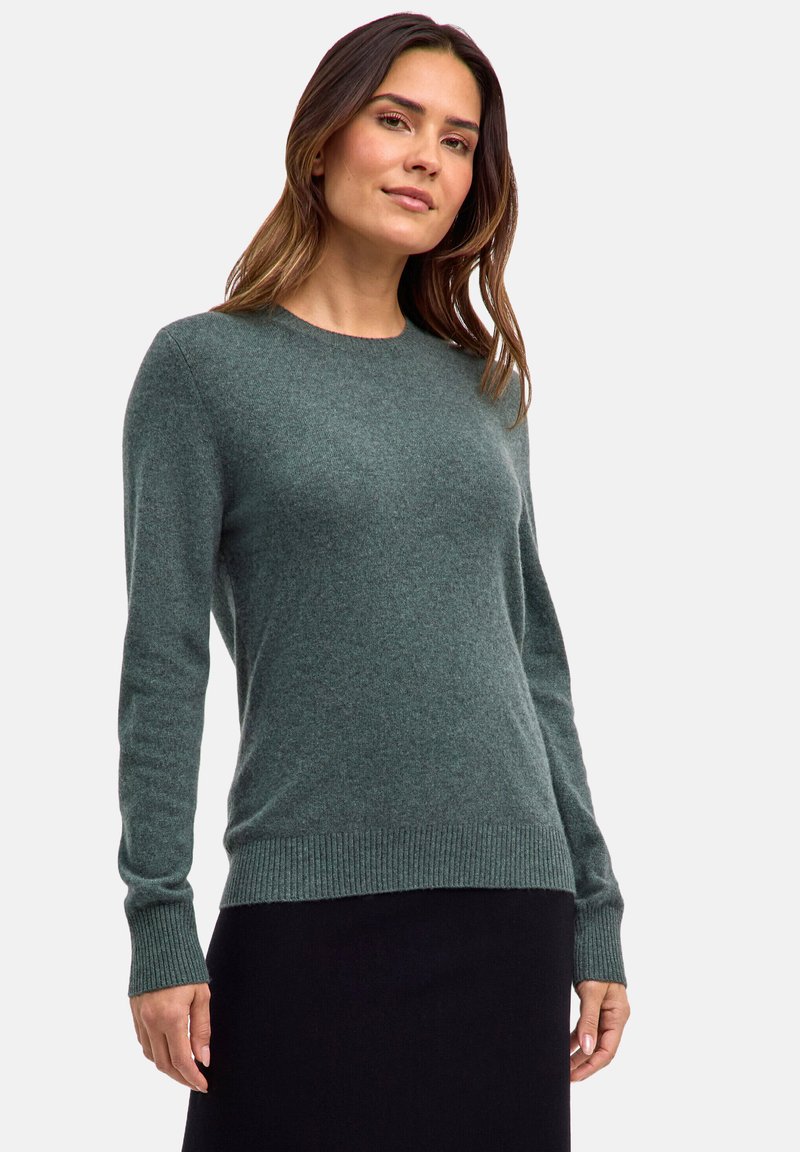 Grüner, langärmeliger Pullover aus weichem Strickmaterial. Hat einen Rundhalsausschnitt sowie gerippte Bündchen und Saum. Strukturiertes Gewebe mit einem dezenten Muster.