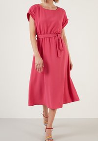 Korallfärgad knälång klänning med korta ärmar, cinchad midja och tygbälte. Slät textur med en lös, flödande silhuett.