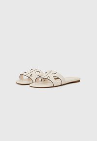 Sandales à glissière beige avec deux larges brides dotées de découpes noires. Semelle lisse et plate.