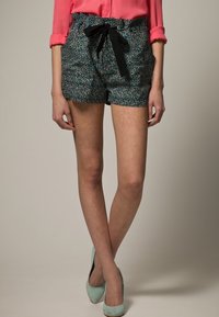 Korte broek met een bloemendessin in donkerblauw en groen, met een zwart lint dat om de taille is geknoopt. De broek heeft een ontspannen pasvorm en zijzakken.