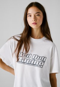 T-shirt en coton blanc avec un graphisme "Red Bull Racing" en bleu foncé. Le t-shirt a une coupe décontractée et des manches courtes.