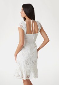 Abito bianco in pizzo con maniche corte a sbuffo, schiena scoperta, tessuto testurizzato, intricato motivo floreale e orlo arricciato.