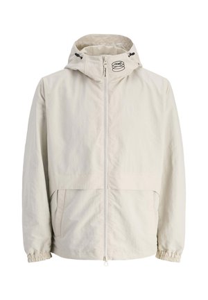 Veste à capuche couleur beige clair fabriquée en matière légère. Elle possède une fermeture éclair à l'avant, des poignets élastiques et un logo sur la capuche.