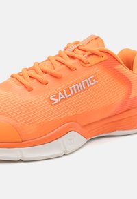 Narancssárga sportcipő hálós felsőrésszel, texturált dizájnnal, fehér "SALMING" logóval és párnázott talppal. Jellemzője a passzoló narancssárga cipőfűző és díszítések.