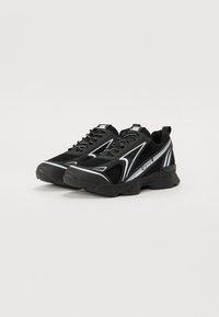 Black athletic shoes with a mesh upper, contrasting white accents, lace-up design, thick sole, and curved lines along the sides.