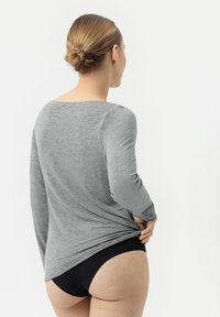 Chemise grise à manches longues en tissu doux, avec un décolleté arrondi et des bras ajustés, associée à un sous-vêtement noir. Design simple et discret.